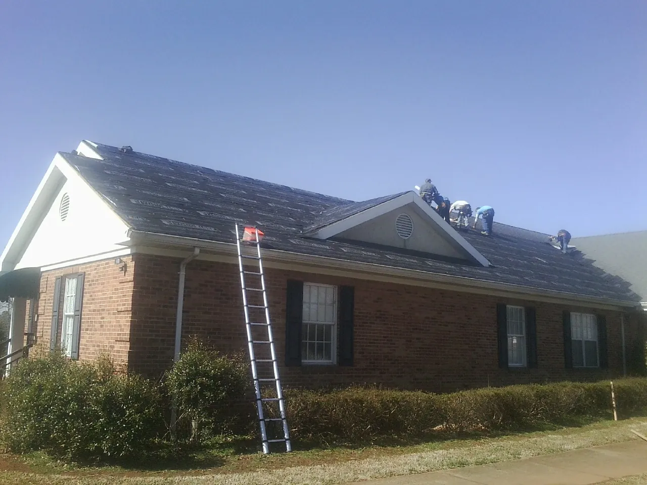 Crew tearing shingles off a brick ranch roof with a ladder set — Metal Roof Repair work by our crew in Hernando