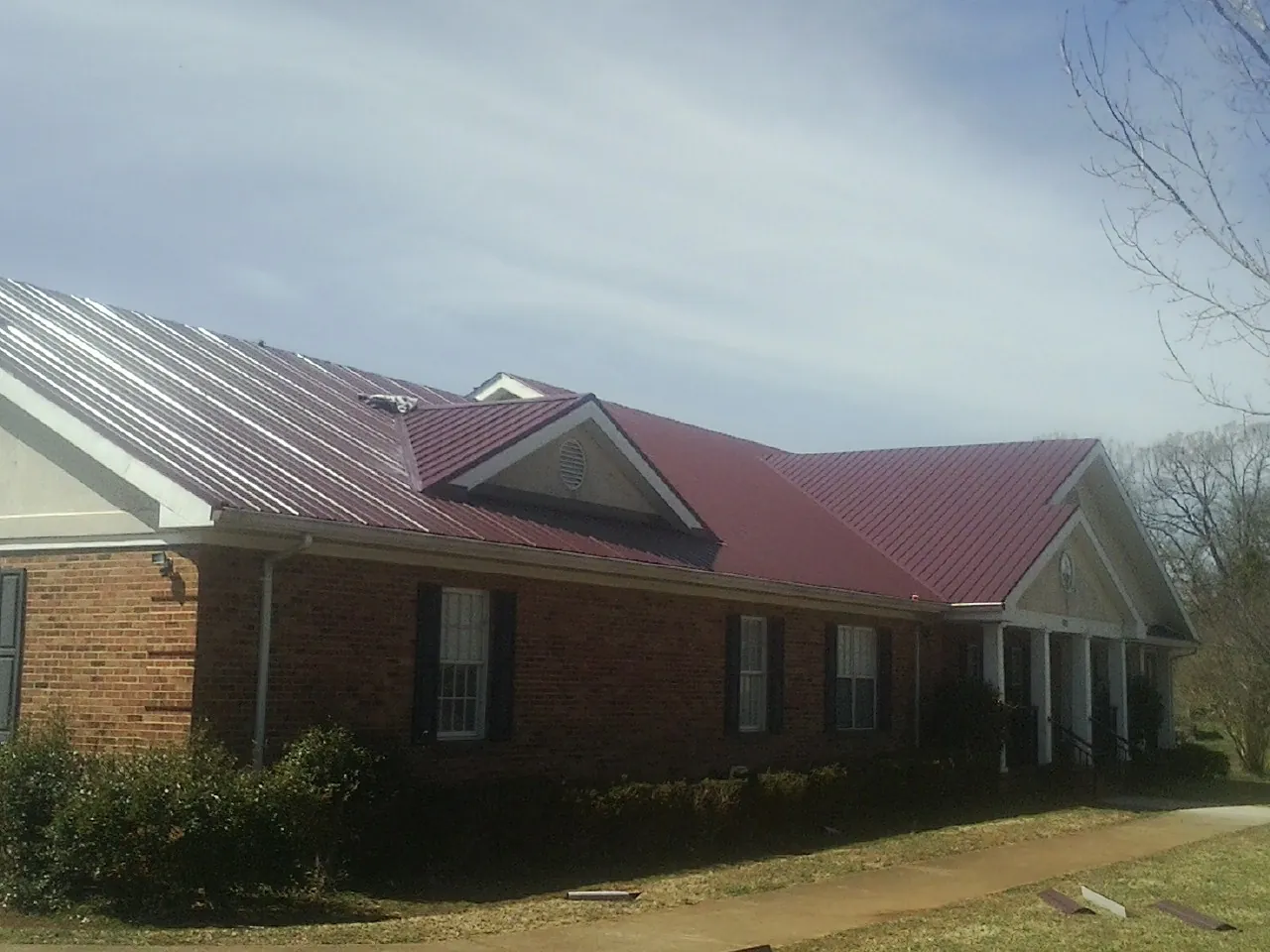 Red metal roof with gabled entries on a long brick building, from a Hail Damage Roof Repair job in Hernando