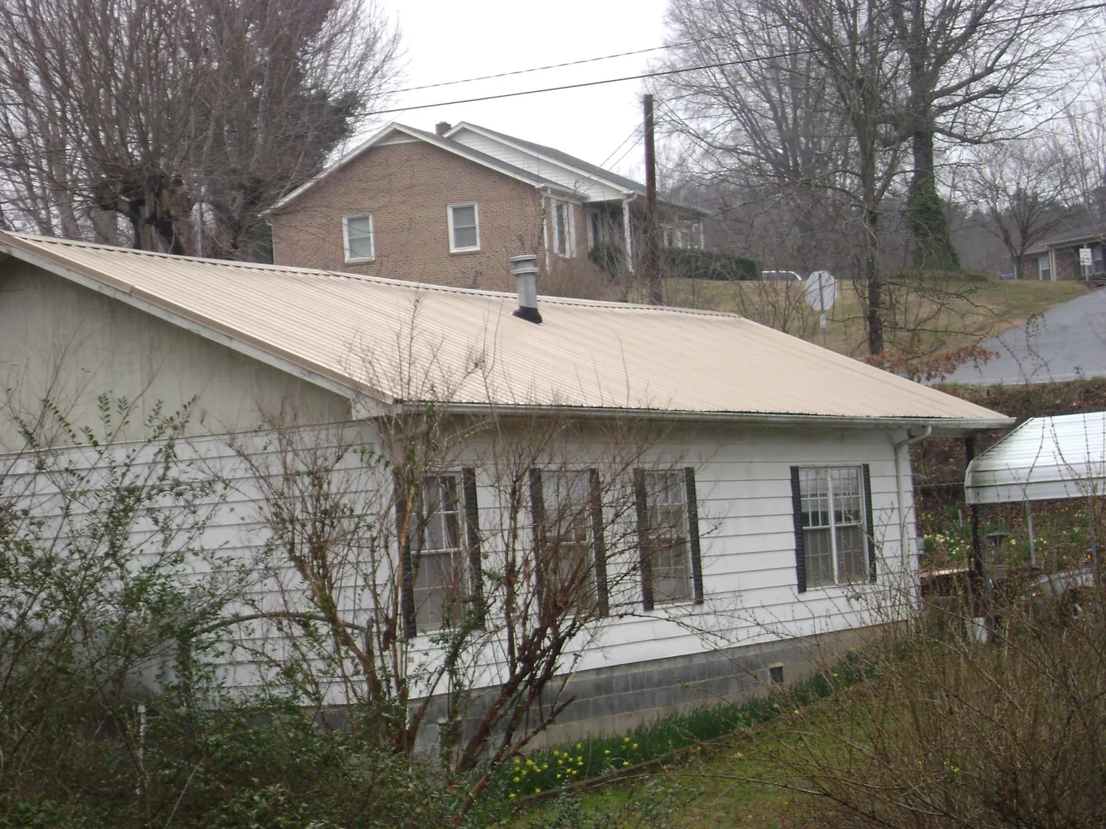 Tan metal roof on a white sided house set into a hillside — Commercial Roofing by Roofing Brothers in Hernando