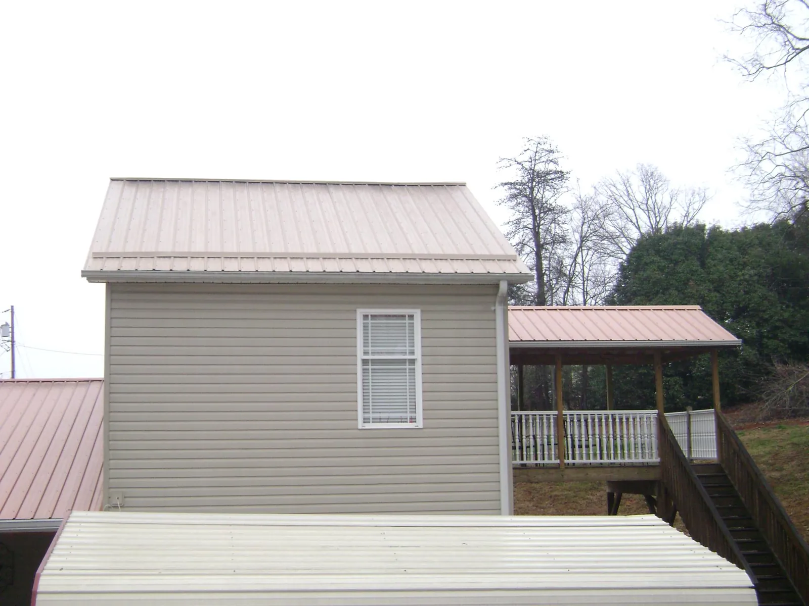 Tan metal roofs on a two story addition and attached porch, from a Roof Replacement job in Hernando